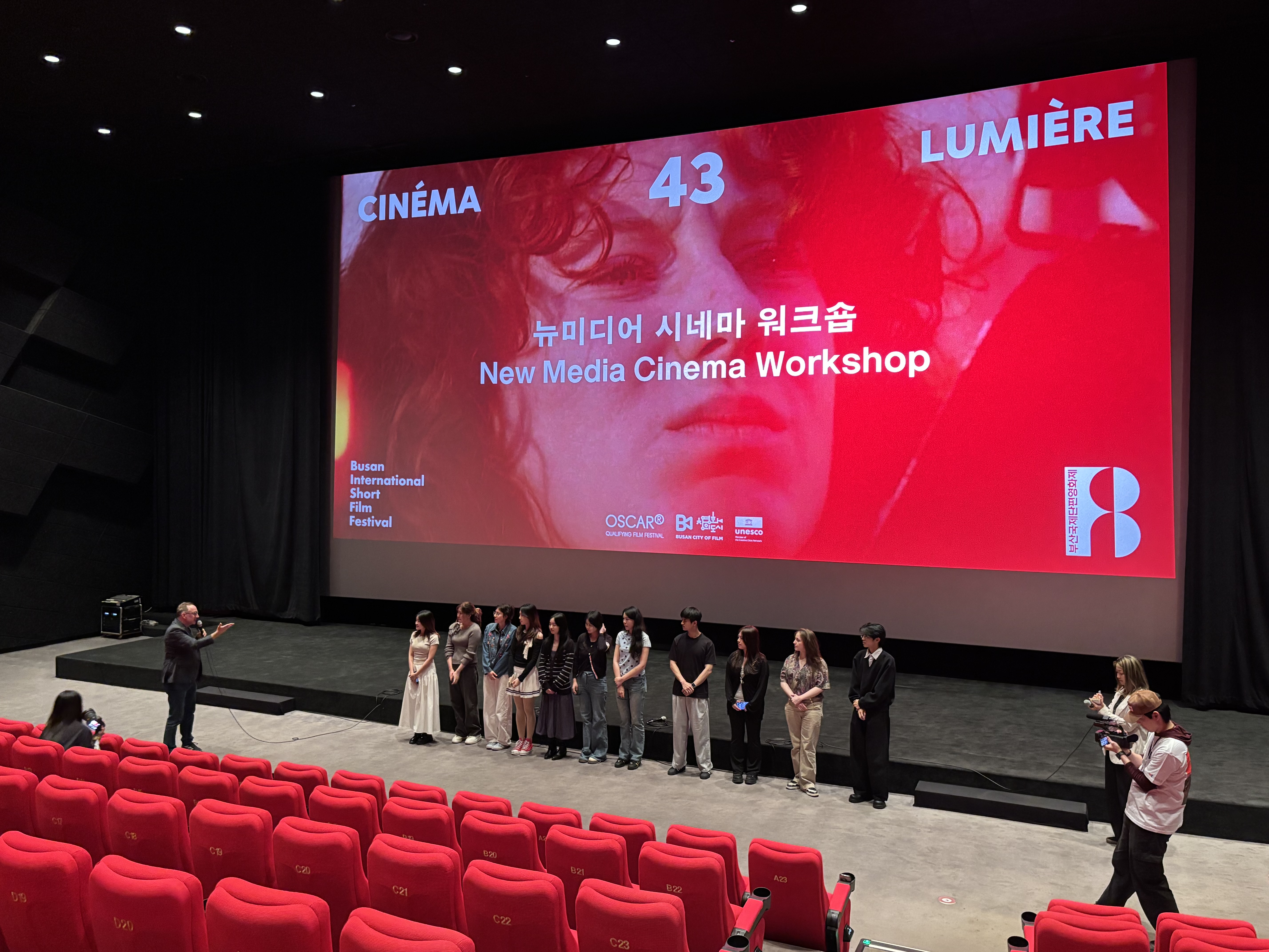 Students and masterclass participants standing in front of the large cinema screen